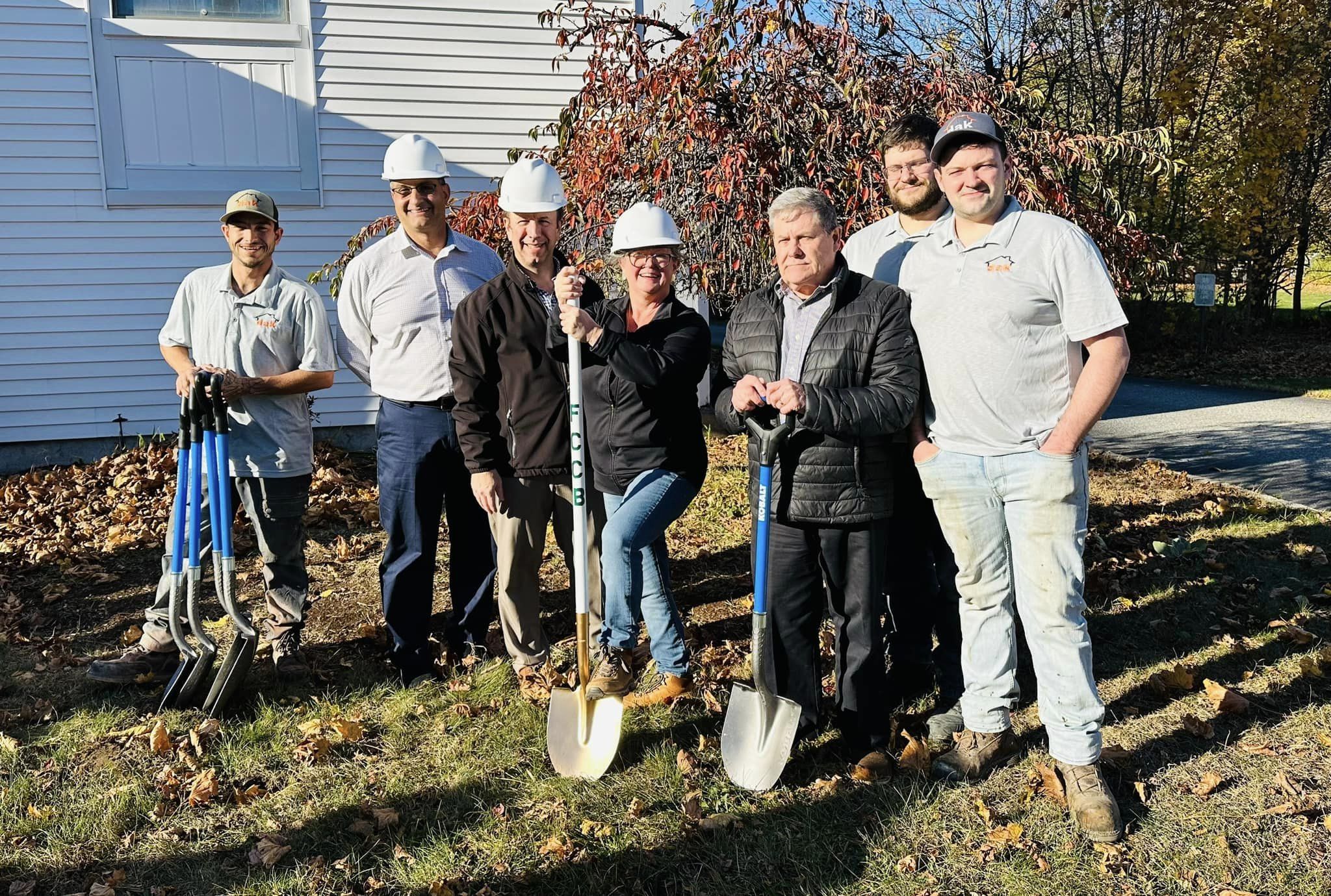 Group of people standing with shovels in front of church at groundbreaking ceremony.